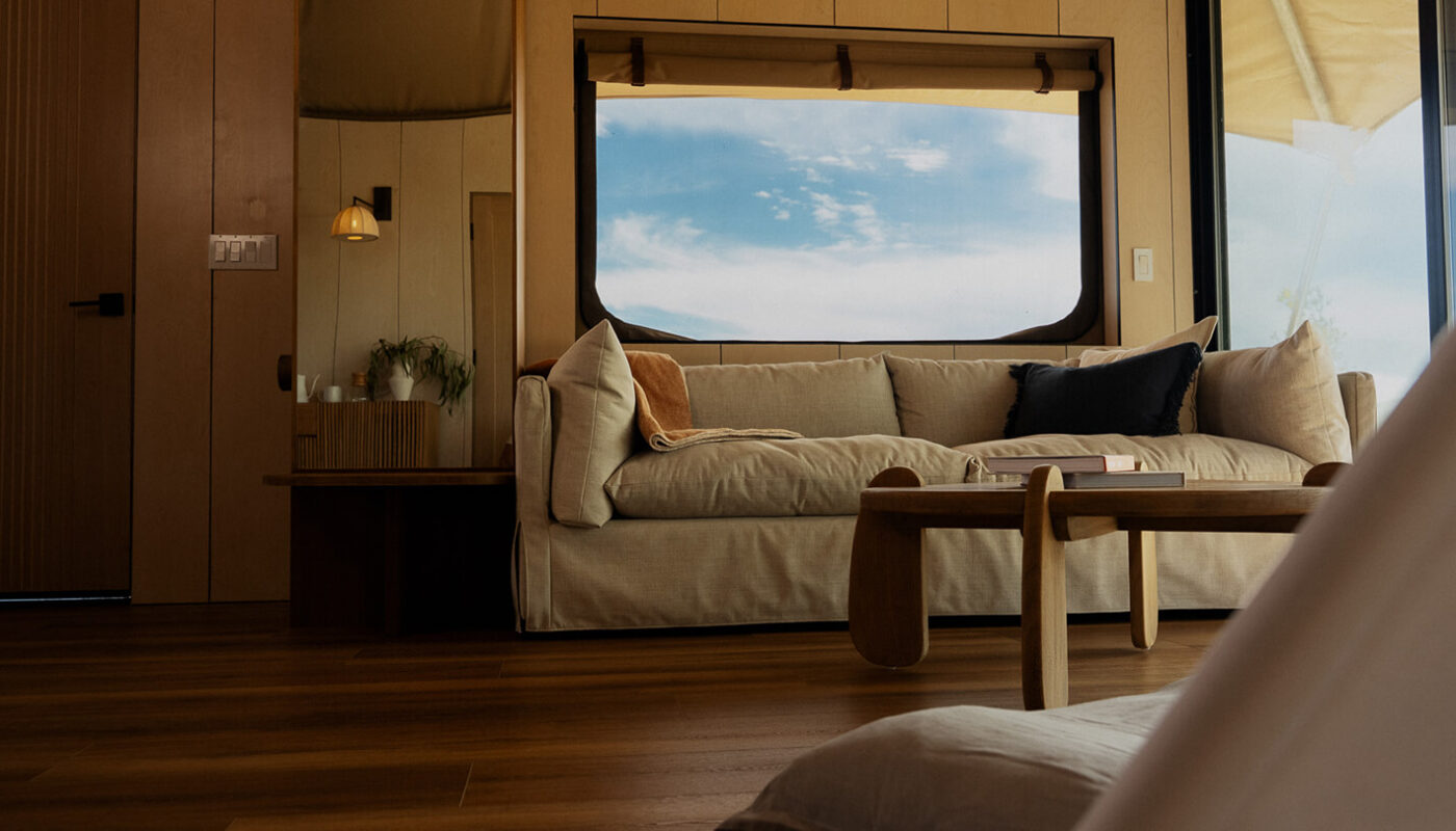 A cozy interior with a beige sofa and wooden coffee table, featuring large windows showcasing a blue sky outside.