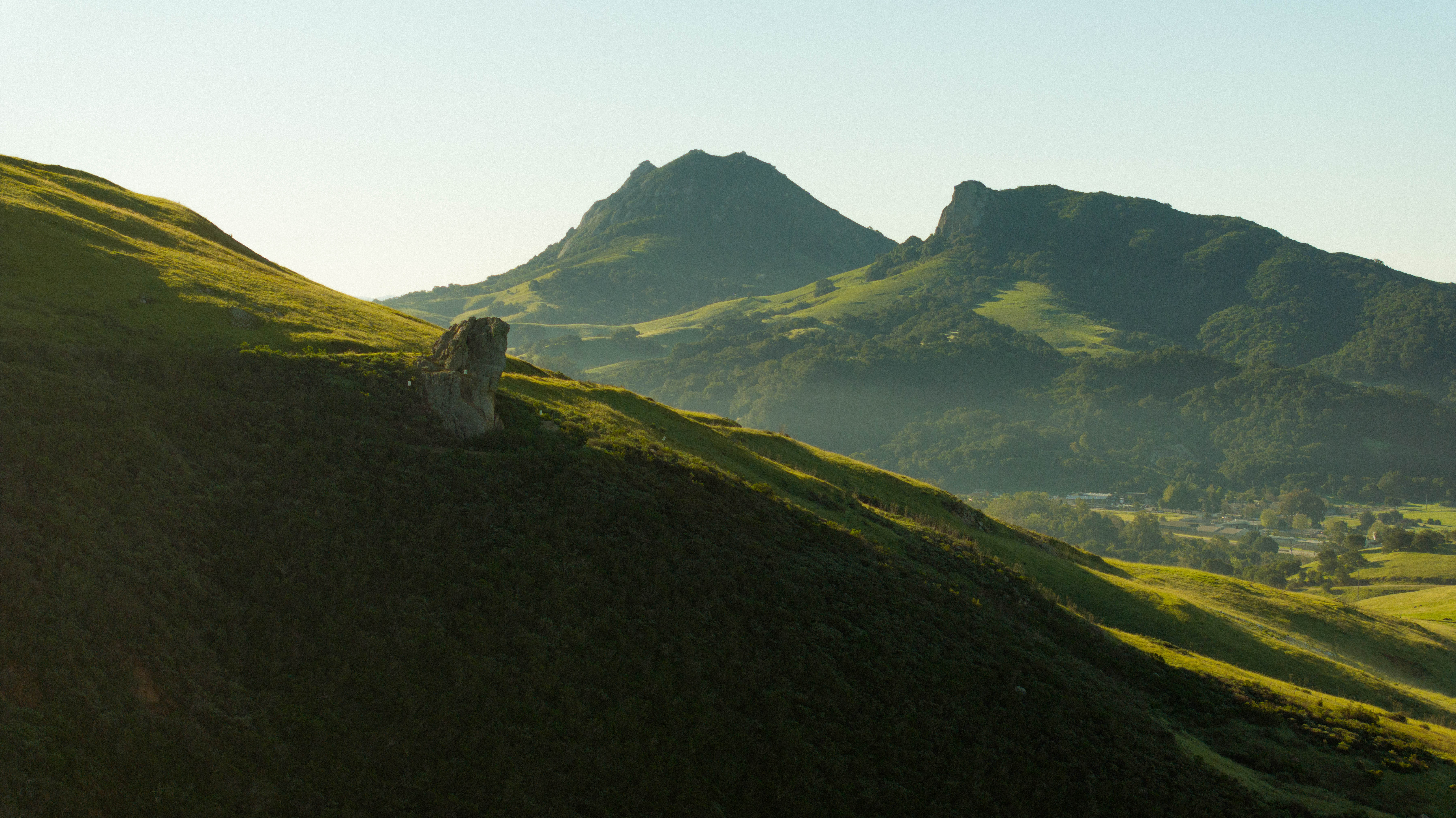 Rolling green hills lead to distant mountains, with a prominent rock formation in the foreground.