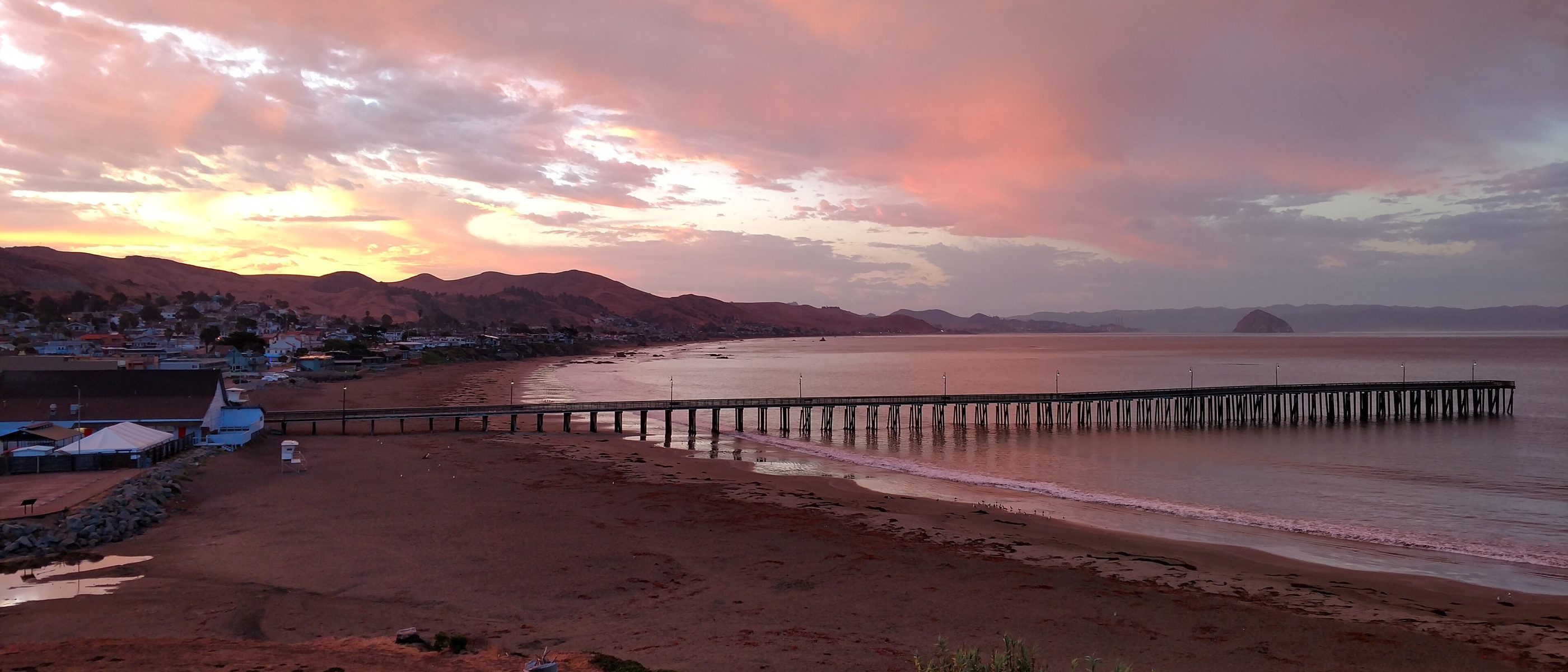 Pink sunrise sky over Cayucos Pier with Morro Rock in the distance