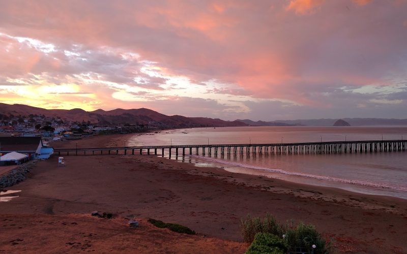 Pink sunrise sky over Cayucos Pier with Morro Rock in the distance