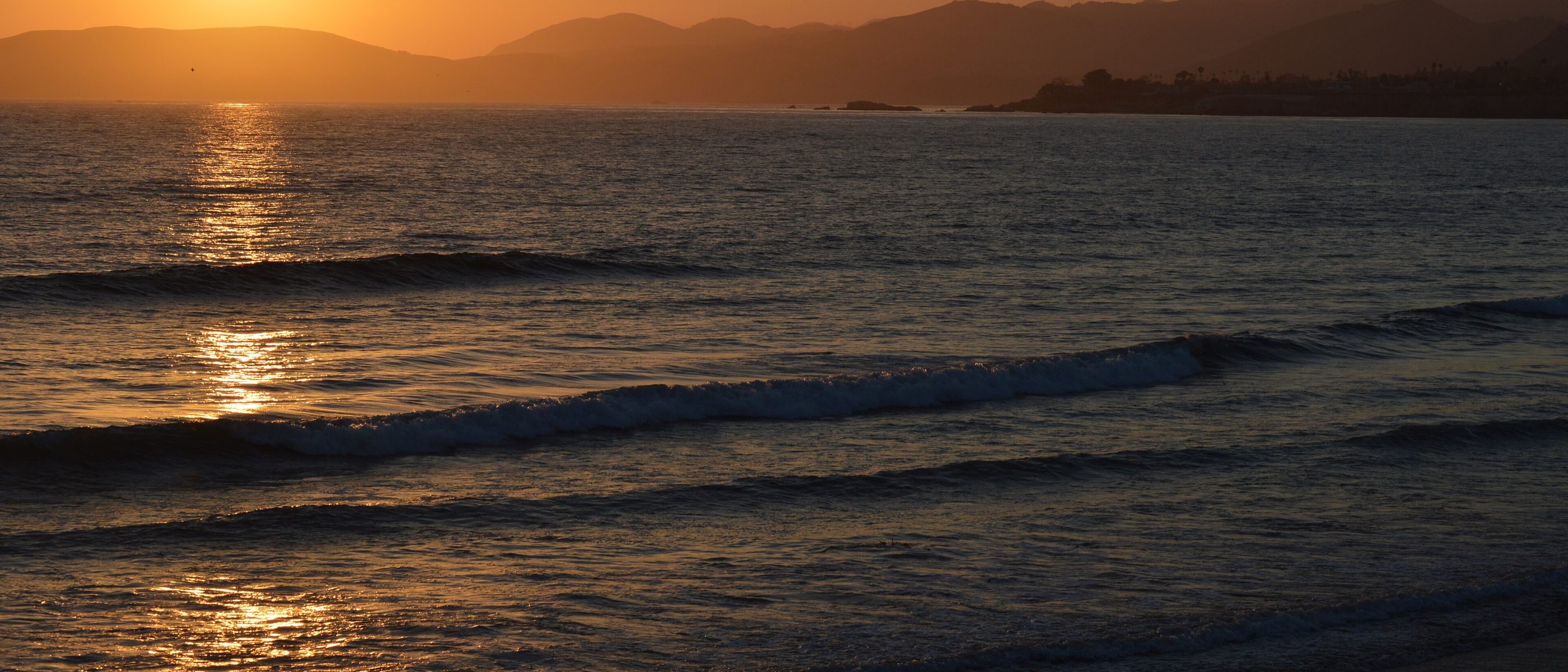 Sun setting over ocean waves and coastal hills at Pismo Beach