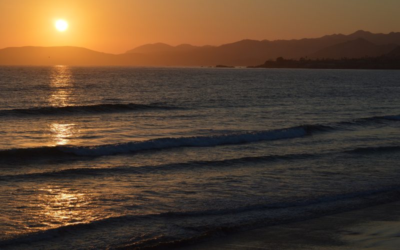 Sun setting over ocean waves and coastal hills at Pismo Beach